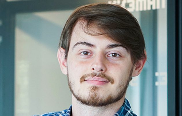 young bearded man with fair skin smiling faintly into camera