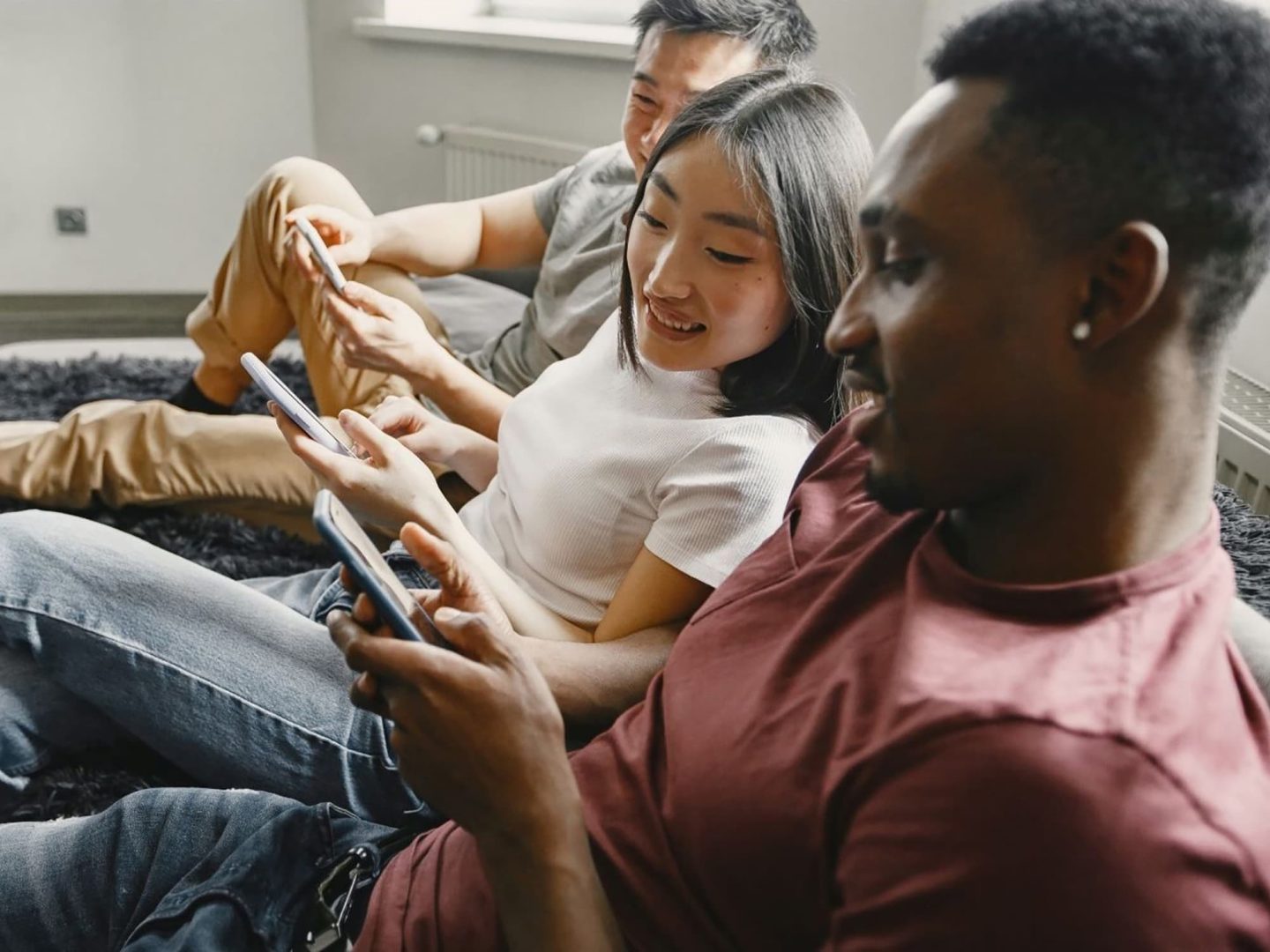 trio of young mobile phone users sitting down and looking at their phones