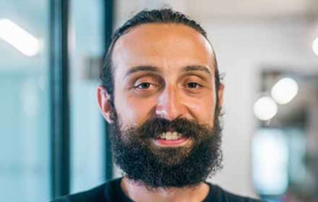 young man with beard looking and smiling into camera