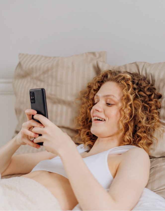 image of red-headed women smiling at her phone in bed