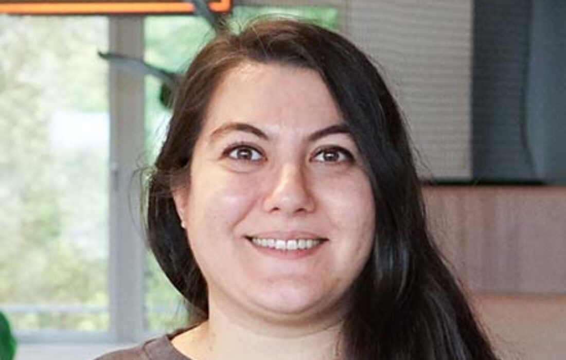 young woman with long dark hair smiling into the camera with office backdrop