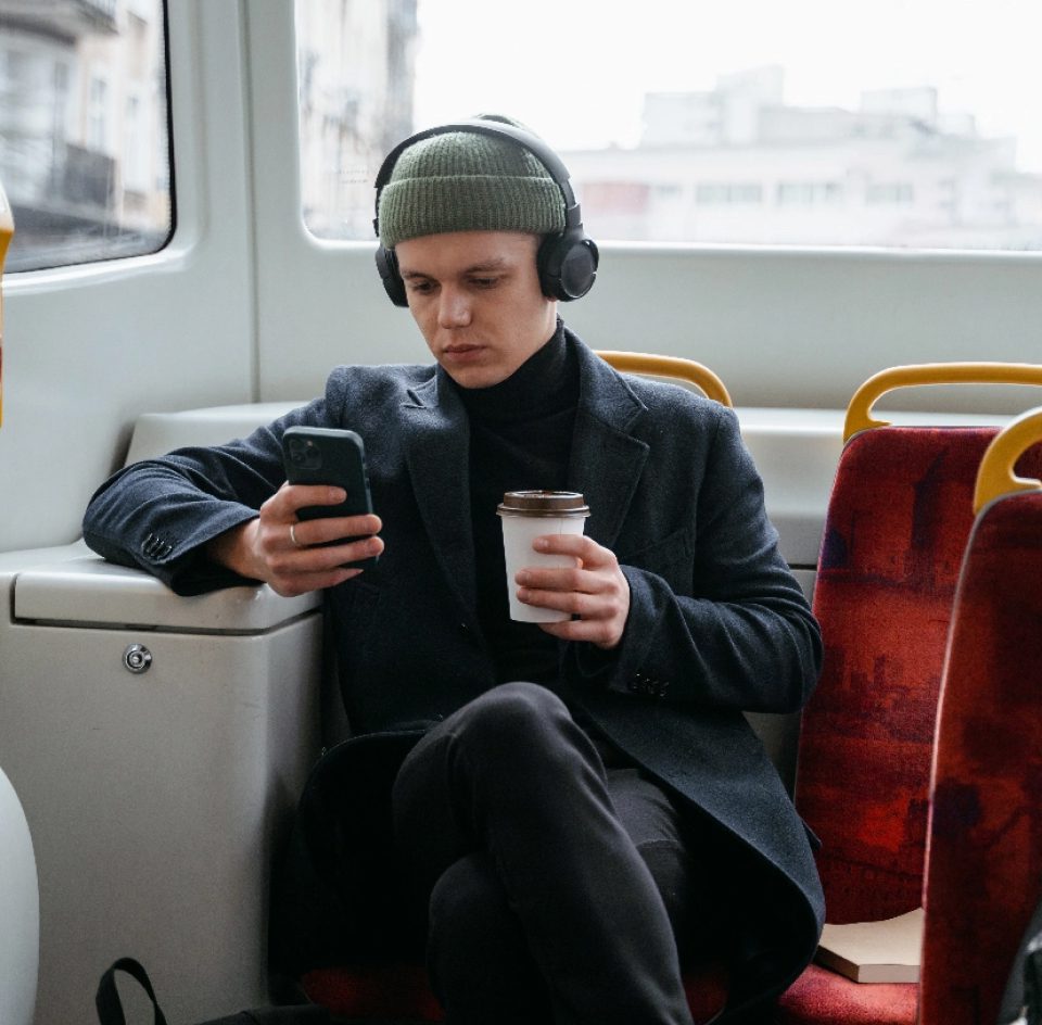 Young man with hat and headphones on looking at his phone on public transport