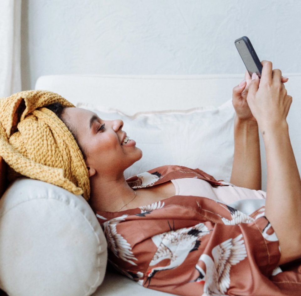 Young woman lying on a sofa smiling up at her smartphone