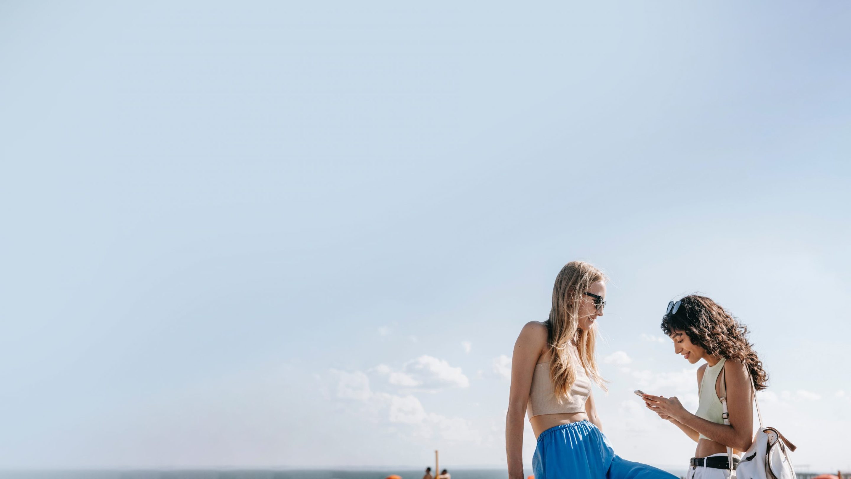 two young women looking at the phones against a blue sky backdrop