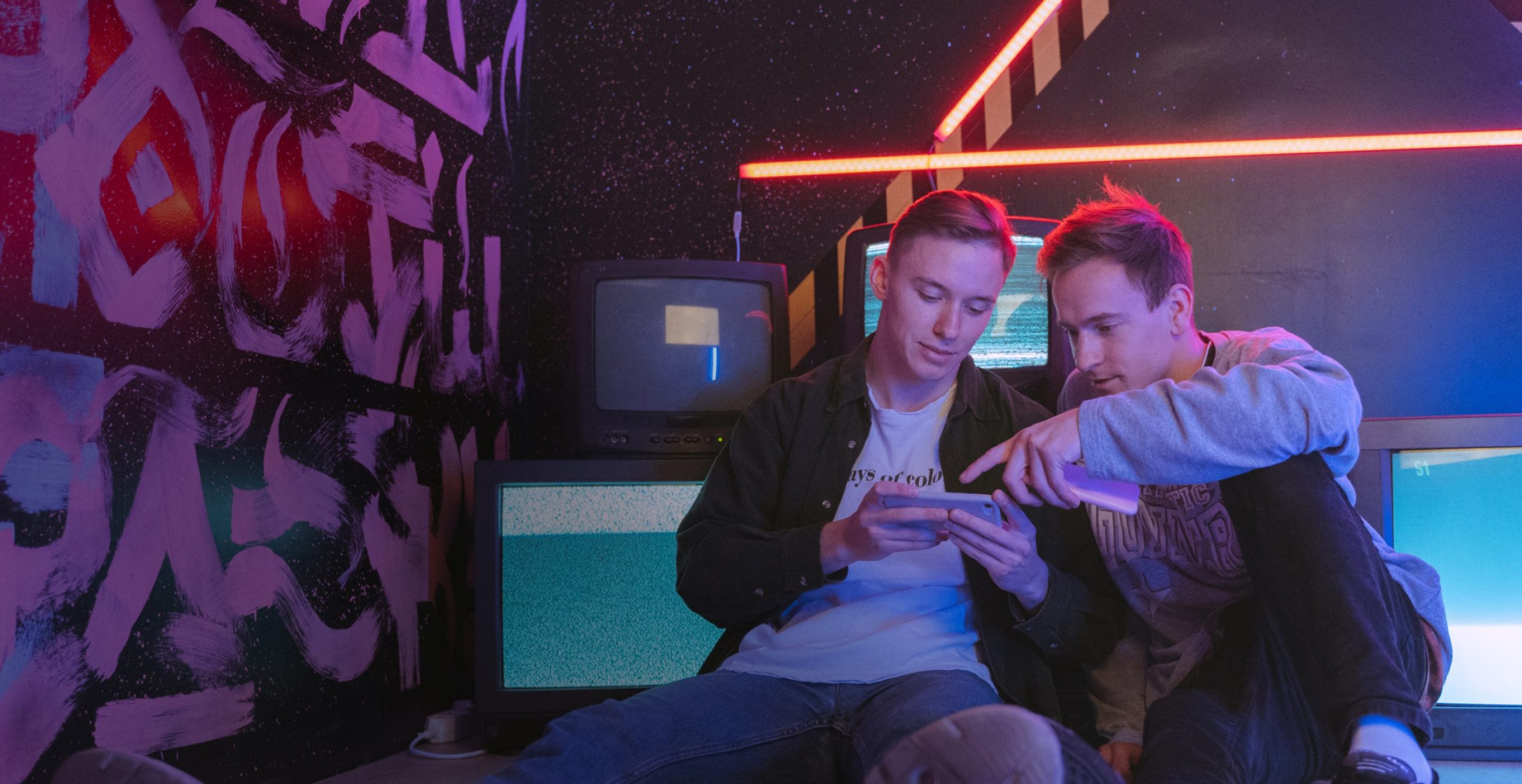 two men sitting down playing mobile games in a dark room