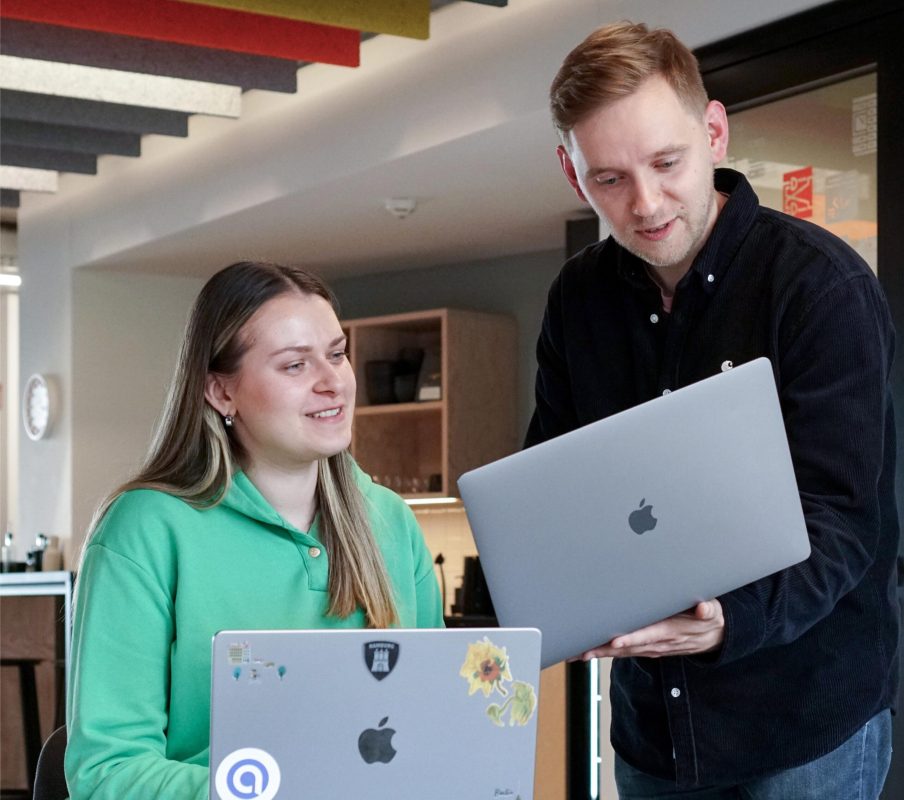 midshot of two developers showing each other their laptops and smiling