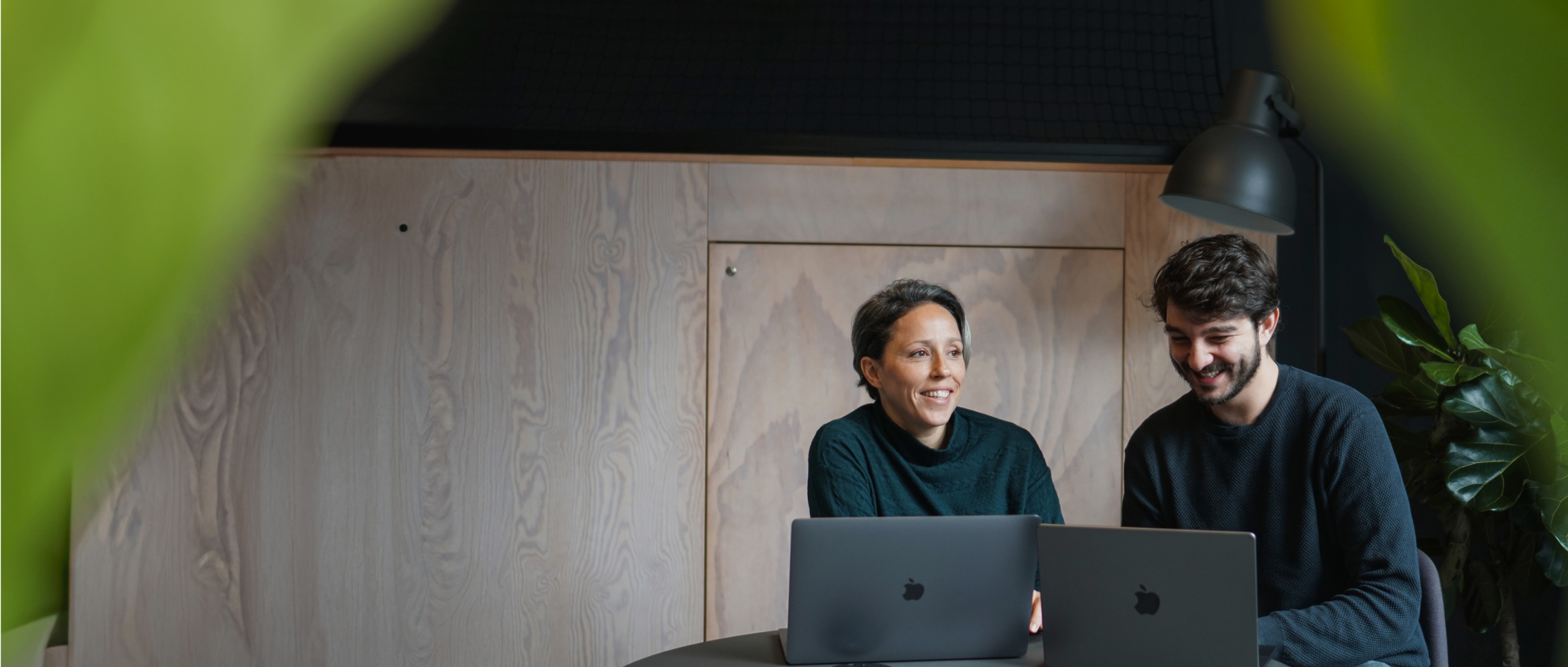 two young people sitting in a room smiling at their laptops